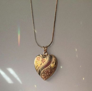 Gold heart locket with flowers and swirly engravings hanging on a gold chain