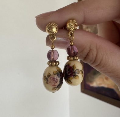 Gold toned beaded earrings with purple and cream colored beads with a printed floral design