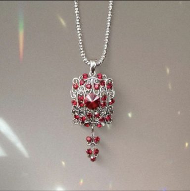Silver toned rectangular filigree pendant with deep red crystals and a hanging crystal detail